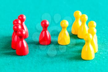 concept scene - few red pawns with leader in front of several yellow pawns with leader on green baize table
