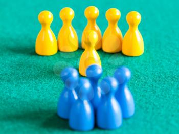 concept scene - few yellow pawns with leader in front of blue pawns on green baize table. Focus on yellow leader