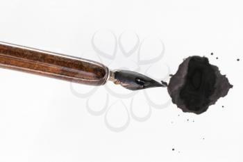 top view of black painted nib of brown penholder over ink blot on white paper