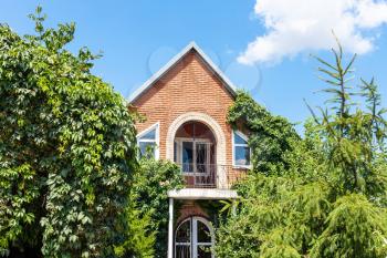 facade of country brick house and green trees in ornamental garden in sunny summer day in Kuban region of Russia