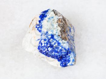 macro shooting of natural mineral - raw Lazurite (Lapis Lazuli) gemstone on white marble from Ural Mountains