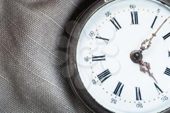 clock face of vintage pocket watch on gray textile background close up
