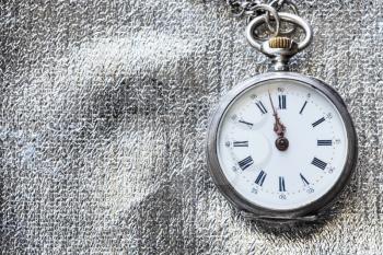 two minutes to twelve o'clock on antique pocket watch on silver textile background