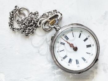 two minutes to twelve o'clock on old pocket watch with chain on white concrete background