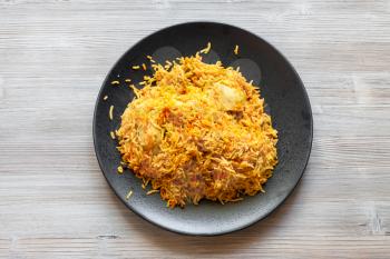 Indian cuisine - Murg Sindh Biriyani spicied chicken pulao cooked with potato in DUM style in tandoor on black plate on wood board