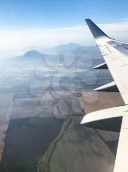 view of aircraft wing and North Caucasus mountains near Pyatigorsk city in Stavropol Krai of Russia from the airplane porthole in flight in september day