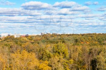 white clouds in blue sky over colorful forest of Timiryazevskiy park and urban houses in Moscow city in sunny october day