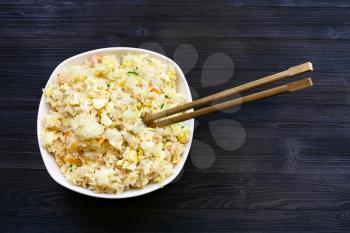 Chinese cuisine dish - top view of portion of Fried Rice with Shrimps, Vegetables and Eggs (Yangzhou rice) with chopsticks on dark wooden table
