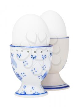 side view of pair white boiled eggs in ceramic egg cups isolated on white background, the egg with a pointy end up on foreground