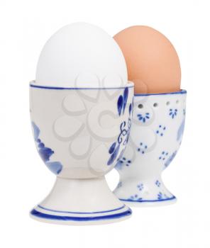 side view of pair of boiled eggs in ceramic egg cups isolated on white background, the white egg on foreground