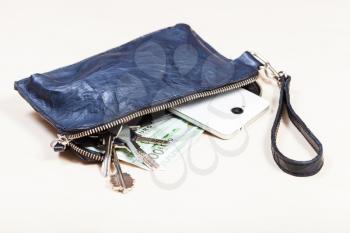 open blue leather wristlet purse bag with bunch of keys, smartphone and euro banknotes on pale brown table