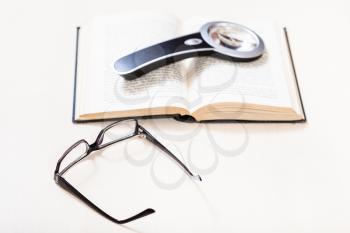 reading book with low vision - eyeglasses and magnifier on open book on pale table (focus in the foreground)