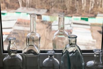 many empty bottles on windowsill and view of city yard through home window on sunny spring day on background