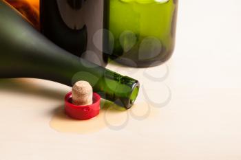 overturned cognac bottle and cork near empty wine bottles on wooden board