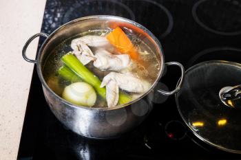 above view of chicken wings broth is boiled in steel stewpot on stove at home kitchen isolated on white background