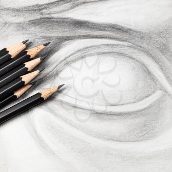 square view of set of black graphite pencils on hand-drawn academic drawing of plaster cast eye close up