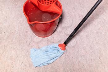 mop cleans linoleum flooring near red bucket with water at home