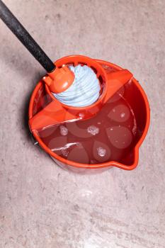 top view of squeezing mop in red bucket with dirty water at home
