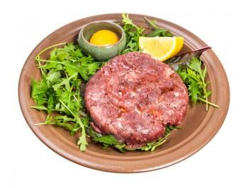 portion of Steak tartare (raw minced beef meat and raw yolk in bowl on fresh greens) on brown plate isolated on white background