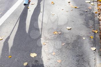 shadow of walker of Nordic walking on footpath in city park on sunny autumn day