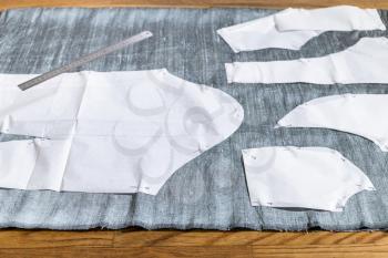 paper sewing pattern layouts of dress and steel ruler on gray fabric on wooden table at home