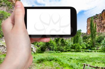 travel concept - tourist photographs of green meadow in Ihlara Valley of Aksaray Province in Cappadocia in spring in Turkey on smartphone with empty cutout screen with blank place for advertising