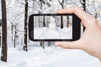 travel concept - tourist photographs of snowman at snowy meadow in winter morning on smartphone in Moscow, Russia
