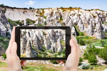travel concept - tourist photographs of rural landscape with ancient cave churches near Goreme town in Cappadocia on smartphone in Turkey in spring