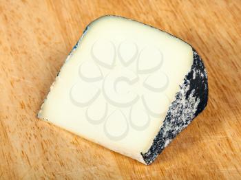 piece of local italian Perla Nera sheep's milk cheese on light wooden cutting board