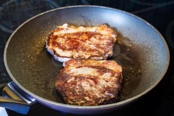 two fried piece of meat in frying pan on ceramic electric range at home kitchen