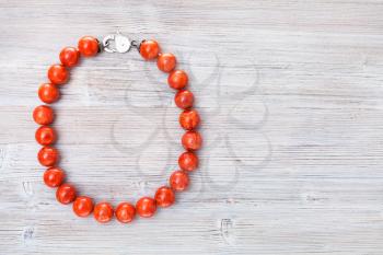 top view of red coral necklace on gray wooden board with copyspace