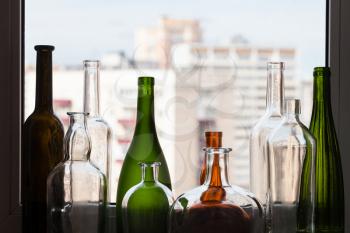 various empty bottles on windowsill and view of city through home window on background