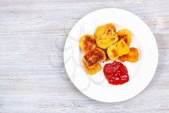 top view of fried chicken nuggets with ketchup on white plate on gray wooden board