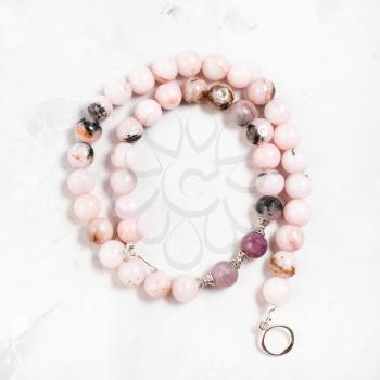 coiled necklace from cherry blossom rose quartz beads on gray concrete surface