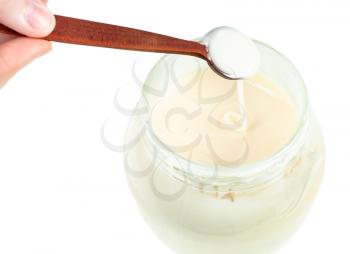 above view of natural organic white honey pouring from little wooden spoon into glass jar with honey isolated on white background