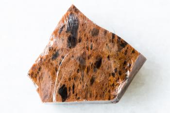 closeup of sample of natural mineral from geological collection - unpolished Mahogany Obsidian rock on white marble background
