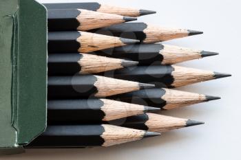 sharp tips of set of black graphite pencils close up in green cartboard box on white background