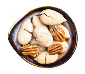 top view of cracked and shelled pecan nuts in ceramic bowl isolated on white background