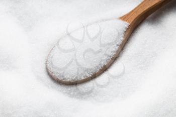 above view of wooden spoon with sugar substitute - crystalline extract of stevia plant close up on pile of sugar