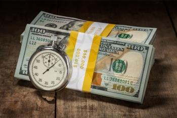 Time is money loan concept background - stopwatch and stack of new 100 US dollars 2013 edition banknotes bills bundles on wooden background