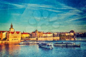 Vintage retro hipster style travel image of Vltava river with tourist boats and Prague Stare Mesto embankment view from Charles bridge on sunset with grunge texture overlaid. Prague, Czech Republic