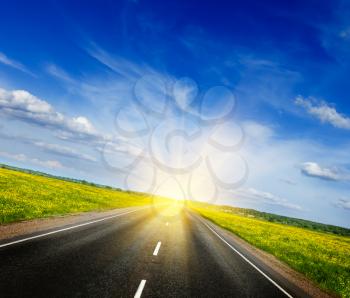 Travel concept background - road in blooming spring meadow on sunset