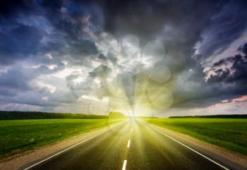 Travel concept background - road and stormy dramatic sky on sunset