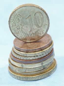 Ten euro cent coin balancing on a top of coins stack on a blue background.