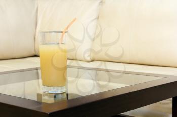 Glass juice on transparent table against white leather sofa.