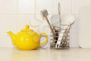 Yellow ceramic teapot and kitchen utensil on white kitchen table taken closeup.