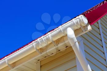 New plastic rain gutter system with drainpipe against blue sky.