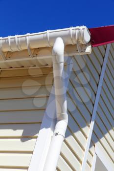 New plastic rain gutter system with drainpipe on white wall taken closeup.