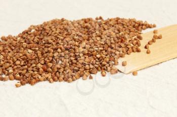 Buckwheat and wooden spoon on a rough white fabric background.