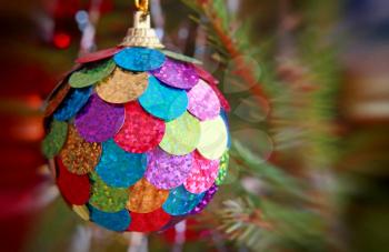 Multicolored Christmas ball on pine branch taken closeup with soft bokeh.